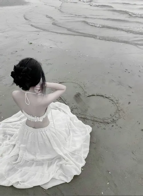 Nàng diện váy trắng mỏng ngồi trên cát che mặt bằng tay cổ thon và bờ ngực lấp ló hút mắt
