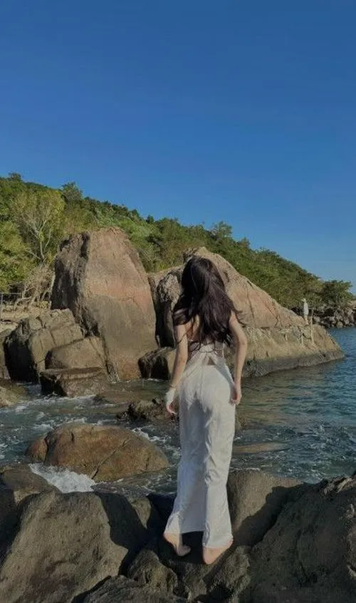 Ảnh bikini che mặt đứng trên đá đen sóng đánh sau lưng đùi thon và hông tròn nổi bật