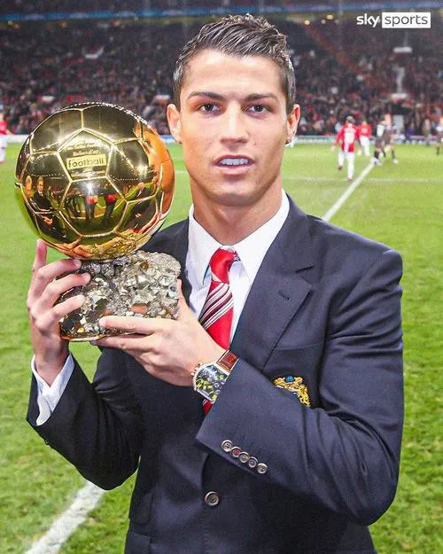 6 Trên sân cỏ, suit chỉnh tề giơ quả bóng vàng trước khán đài, không khí trang trọng rõ rệt.