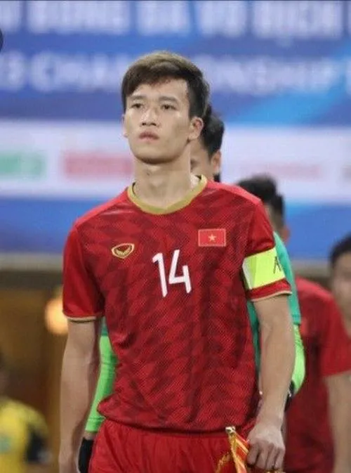 33 Hoàng Đức cúi buộc dây giày, cỏ sân ướt nhẹ, ánh sáng mềm, cảm giác chuẩn bị ra trận