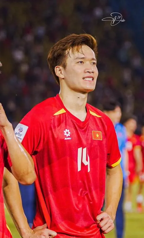 13 Hoàng Đức áo đỏ đội tuyển, dáng đứng tự tin, tóc gọn, ánh mắt hướng lên khán đài