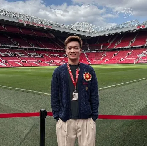 7 Hoàng Đức đứng trước khán đài sân bóng lớn, đeo thẻ, áo khoác, nền sân cỏ rộng mở