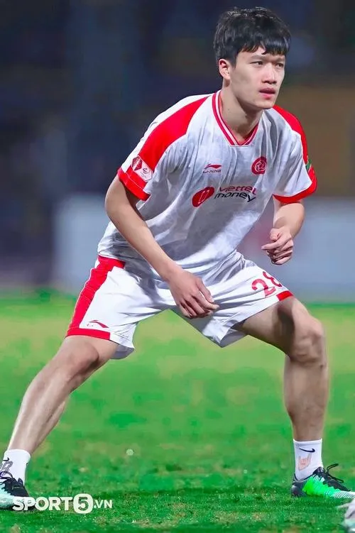 9 Hoàng Đức thi đấu áo trắng đỏ, tư thế phòng ngự, mắt tập trung, bắt dính hành động trên cỏ