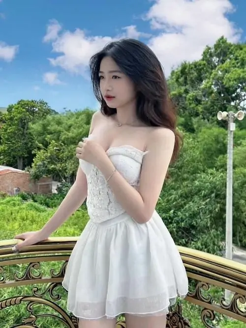 32 Ngoài ban công nhiều nắng, cô gái diện váy trắng bồng ngắn tựa lan can, mái tóc đen uốn nhẹ và dáng đứng chéo chân giúp tổng thể mềm mại, đẹp kiểu ngọt mà vẫn đủ quyến rũ để gây nhớ