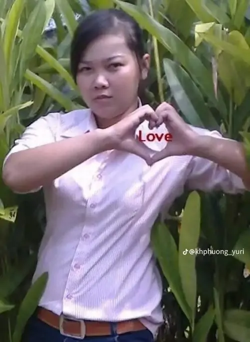 29 Hình gái lạ đời giữa khóm lá xanh với áo tím nhạt và đôi tay tạo hình trái tim, dáng đứng nghiêm túc nhưng nét mặt lại hơi cứng làm khung hình vừa đáng yêu vừa khác khuôn, hợp kiểu ảnh chụp vui ngoài trời