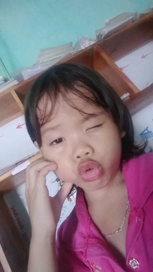 26 Bé gái mặc áo hồng ngồi trên giường, một tay chạm mặt và mắt nheo lại như vừa buồn ngủ vừa làm trò, biểu cảm khó đỡ kết hợp mái tóc rối tạo nên khung hình tươi tắn, lạ lạ nhưng không hề gượng