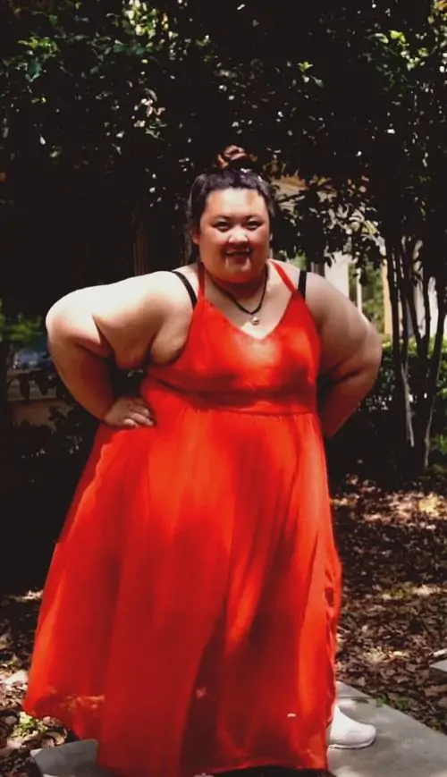 12 Người mặc váy đỏ đứng giữa lối đi cây xanh, chống tay tạo dáng đầy tự tin như đang diễn một phân cảnh của Cô gái xấu xí, màu váy rực và tư thế mạnh khiến ảnh hóa trang này vừa lạ vừa có sức hút riêng