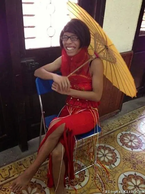 17 Hình nữ lệch góc trong váy đỏ ngồi bắt chéo chân, cầm ô vàng dưới ánh sáng trong nhà, khung cảnh tạo cảm giác như Betty La Fea đang đổi sang phong cách quý cô, vừa duyên dáng vừa có chút diễn xuất rất vui