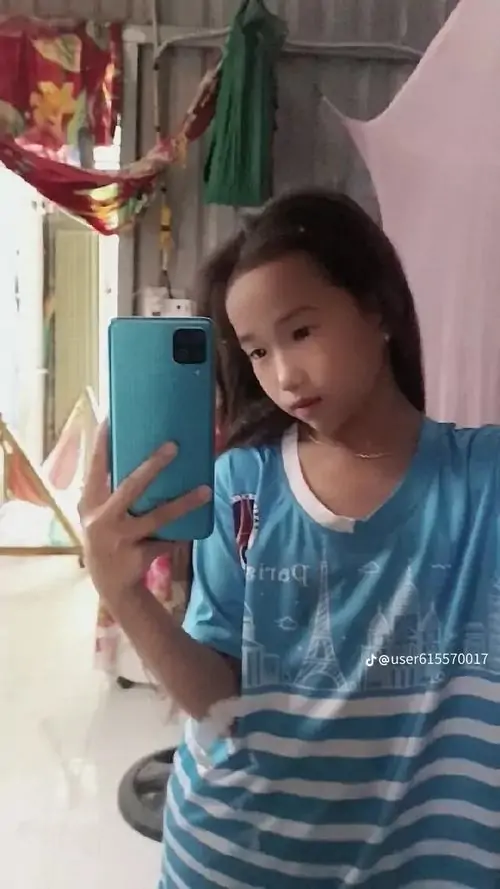 19 Ảnh chân dung nữ qua gương với áo sọc xanh và điện thoại che nửa mặt, góc máy nghiêng làm dáng người mảnh hơn, trong khi biểu cảm tự nhiên giữ lại sự đời thường của một bức selfie chụp chơi đầy ngẫu hứng