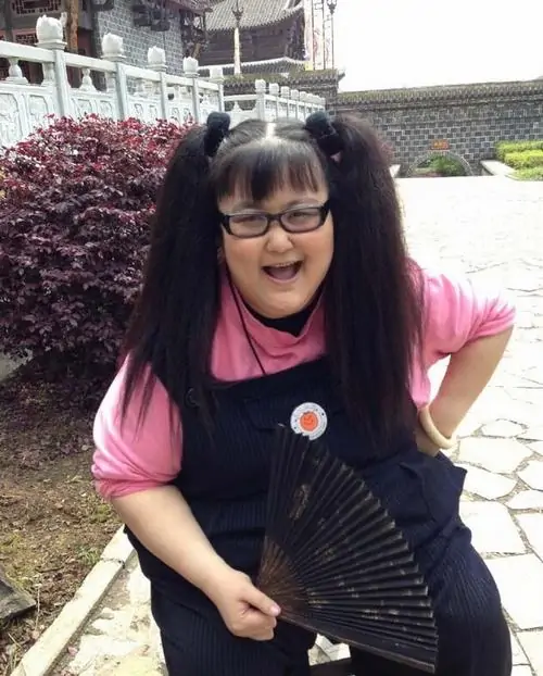 7 Hình nữ lệch góc ngoài sân với kính đen, áo hồng và quạt cầm tay tạo cảm giác như đang nhập vai sân khấu mini, dáng cúi người cùng nụ cười rộng khiến ảnh hài hước này trông rất hoạt náo và có phần khác khuôn