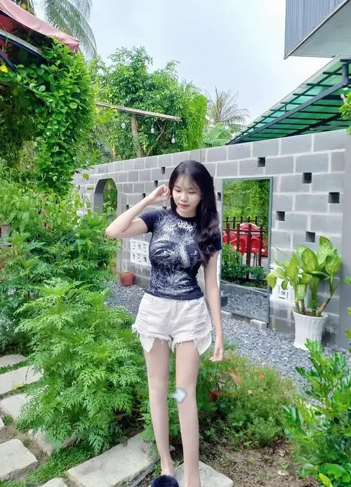 12 Ảnh gái xinh tóc dài đứng giữa khu vườn nhỏ với áo caro tối màu quần short trắng và vẻ ngoài xinh xắn