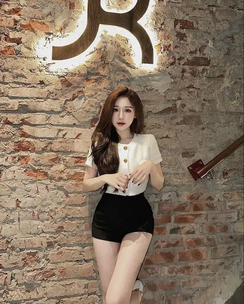 19 Ảnh gái xinh che mặt nhẹ trong set áo trắng quần short đen trước tường gạch mang cảm giác trẻ trung