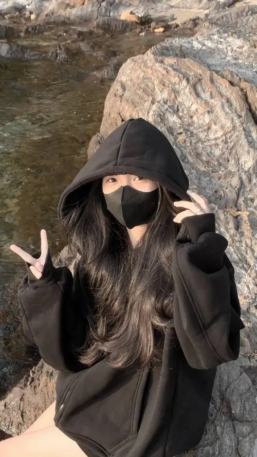 1 Ảnh gái cool mặc áo hoodie đen giữa nền đá ngoài trời, cúi đầu để mũ trùm và mái tóc phủ gần kín gương mặt, hai tay giơ ký hiệu tạo cảm giác ngầu nhưng không lạnh, khung hình đậm chất bí ẩn và rất hút mắt