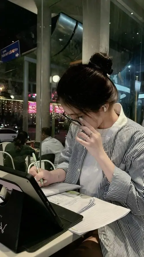 4 Trong quán đêm ánh đèn mờ, cô gái ngồi bên bàn rồi dùng bàn tay che phần lớn khuôn mặt, chỉ để lộ sống mũi và mái tóc sẫm, cách giấu mặt tự nhiên khiến tổng thể trông rất điện ảnh và có chất riêng khó trộn