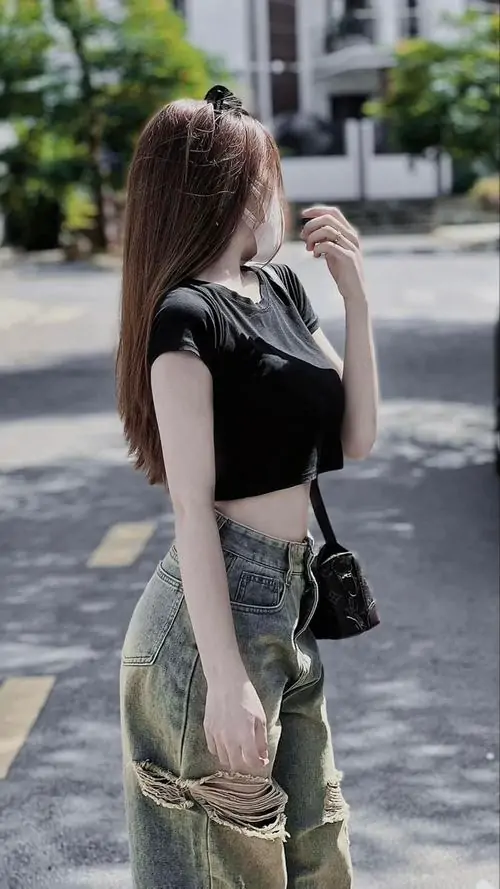 12 Cô gái mặc áo đen và quần xanh đứng bên hè phố, xoay nghiêng người để mái tóc phủ kín phần má cùng nửa mặt, cách giấu gương mặt bằng tóc khiến bức hình mang nét nửa kín nửa hở, trẻ và có độ cuốn rất vừa