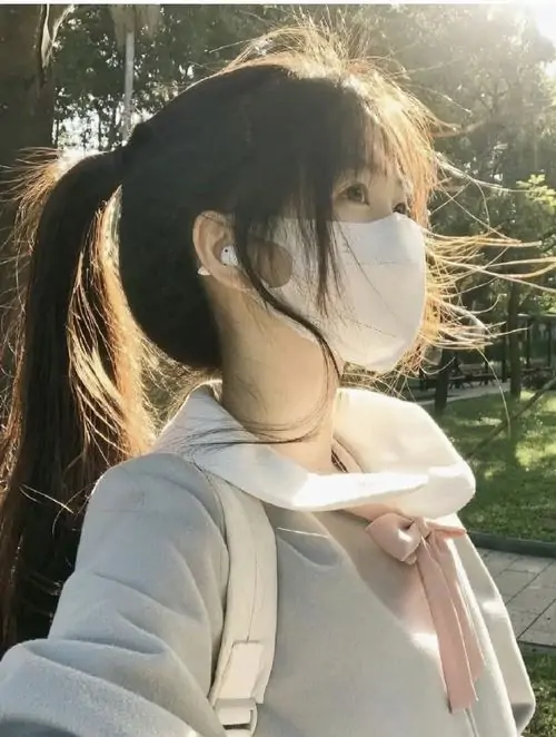 18 Ánh nắng xiên qua hàng cây sau lưng, cô gái đeo khẩu trang trắng rồi nghiêng đầu về phía sáng, phần mặt được che bằng khẩu trang và góc nghiêng mềm, tạo cảm giác trong trẻo nhưng vẫn có nét lạnh rất hợp ảnh thời trang