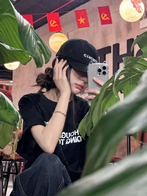 22 Giữa góc quán nhiều lá xanh, cô gái mặc áo đen, đội mũ tối rồi đưa tay lên che ngang phần mặt khi nghiêng đầu, thao tác nhỏ nhưng tạo hiệu ứng rất mạnh, giúp ảnh gái xinh cá tính trông sống động và có nhịp hơn