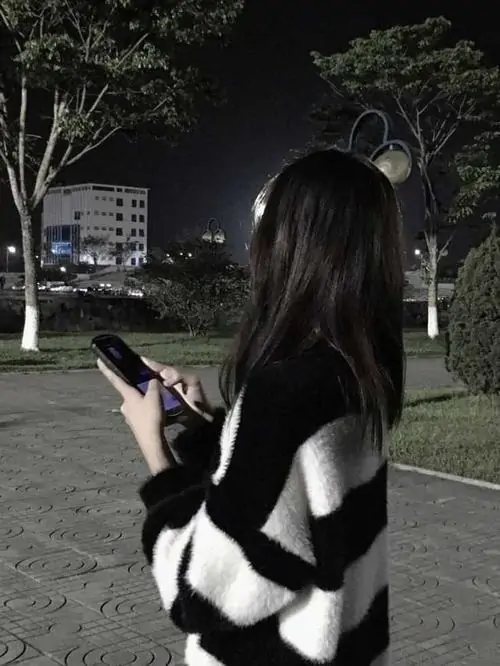 31 Hình cô nàng phố đêm đứng quay lưng dưới trời tối, mái tóc dài phủ kín lưng áo sọc khi một tay cầm điện thoại, cách giấu mặt hoàn toàn bằng tư thế từ phía sau tạo cảm giác lặng, xa và đầy cuốn hút