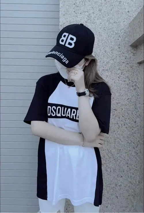 34 Cô gái dựa vào tường sáng màu, đội mũ đen kéo sụp rồi đưa tay lên chạm vành mũ, gương mặt nghiêng nhẹ và phần mắt chìm trong bóng làm bức ảnh giữ được vẻ xinh mà vẫn đậm nét cá tính đường phố