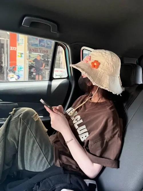35 Ảnh gái vibe Pinterest ngồi trong xe với mũ sáng màu, đưa điện thoại lên che toàn bộ mặt trong lúc nghiêng đầu nhìn màn hình, cách lấy điện thoại làm điểm chắn khiến khung hình hiện đại, gọn và rất hợp ảnh selfie kín mặt