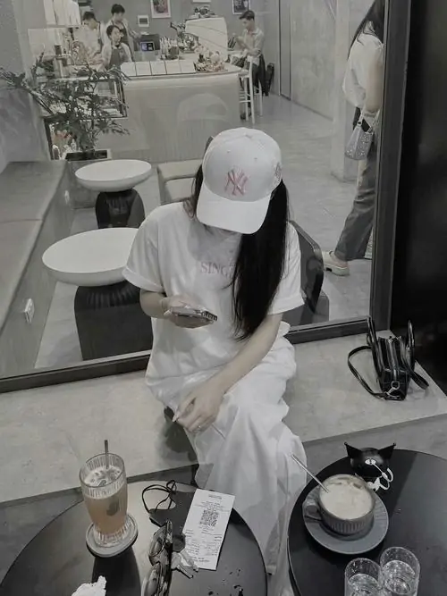 36 Khung chụp tông xám từ trên cao ghi lại cô gái đội mũ trắng trong bếp, cúi đầu làm vành mũ phủ hết khuôn mặt, phần thân hơi gập và tay chống nhẹ tạo cảm giác đời thường nhưng vẫn rất có chất ảnh gái đẹp che mặt