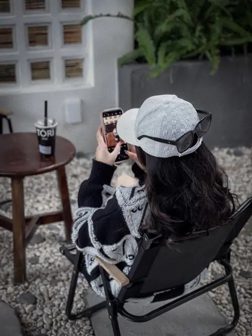 37 Hình gái xinh kín mặt ngồi trên ghế ngoài hiên, đội mũ sáng và quay đầu sang bên để mái tóc cùng vành mũ che gần hết mặt, dáng ngồi thư thả giữa góc quán giúp tổng thể trông mềm, sạch và đầy chất riêng