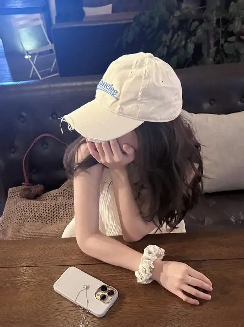 39 Ảnh nữ giấu mặt tựa đầu xuống bàn gỗ, đội mũ trắng và dùng cánh tay chống má che nốt phần mặt còn lộ, ánh sáng thấp làm khung hình thêm mềm, mang đúng cảm giác che nửa mặt vẫn nổi bật và rất cuốn