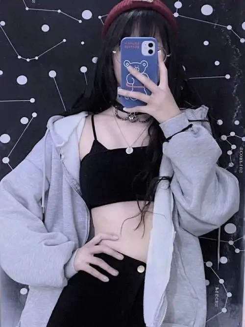 40 Cô gái đứng trước gương với áo khoác sáng và áo trong tối, nâng điện thoại lên chắn trọn khuôn mặt rồi tạo dáng bằng tay còn lại, kiểu che mặt bằng máy chụp quen thuộc nhưng lên hình vẫn cá tính và rất bắt mắt