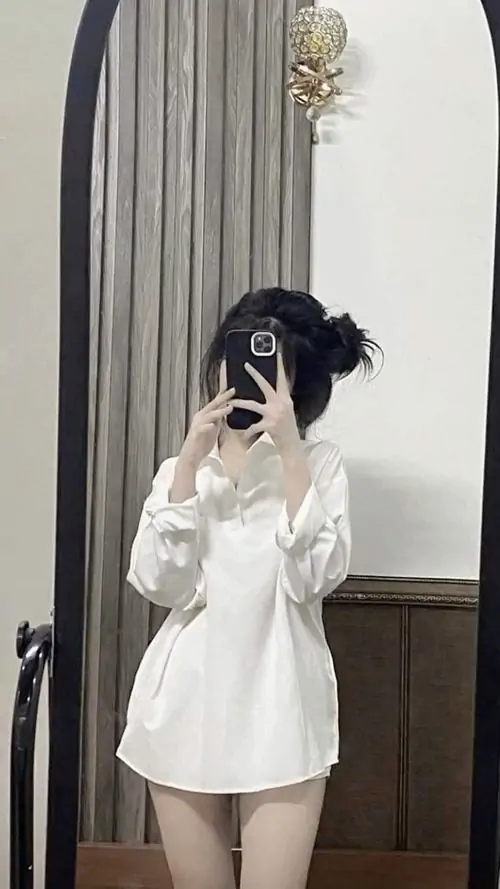28 Đứng trước gương trong góc phòng rèm tối, cô nàng mặc sơ mi trắng rộng và dùng điện thoại che mặt, đôi chân lộ vừa đủ nên vóc dáng vẫn thanh thoát, tổng thể cute kiểu kín đáo mà không hề nhạt