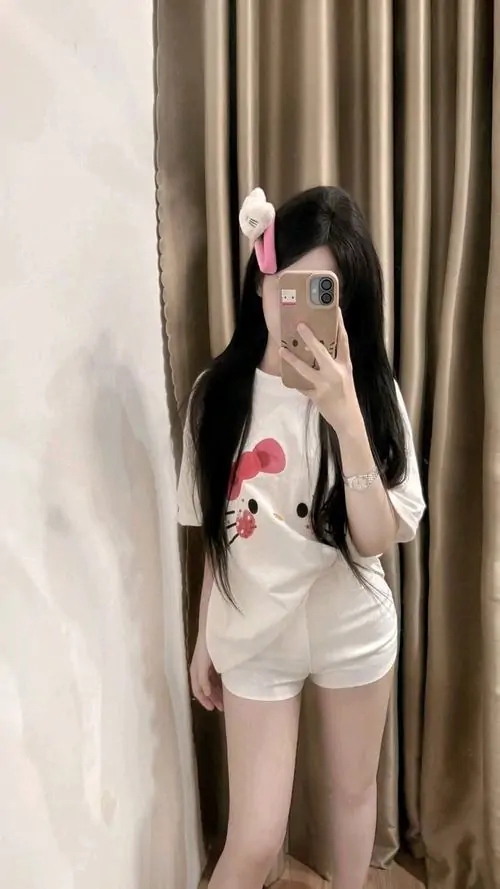 29 Trước gương trong phòng với rèm nâu, nàng phối áo trắng rộng cùng quần ngắn trẻ trung, cách đứng thẳng và tay cầm máy gọn làm bức ảnh đời thường này đẹp hơn nhờ cảm giác gần gũi, tự nhiên