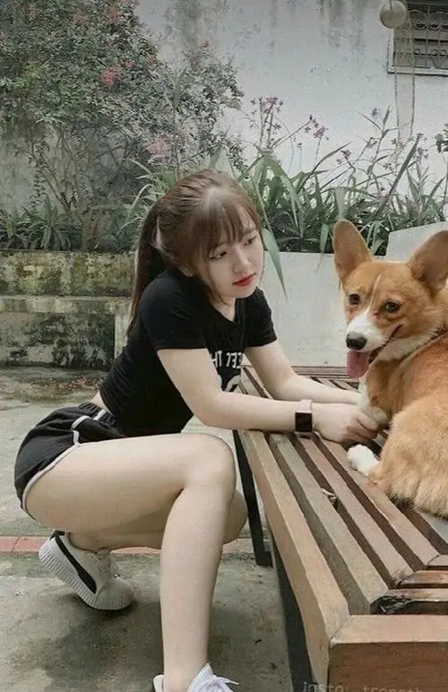 3 Bên ghế gỗ ngoài sân, cô nàng ngồi thấp cạnh chú chó với tư thế hơi nghiêng người, quần ngắn làm đùi và vòng eo hiện rõ, khung hình cute kiểu đời thường mà vẫn giữ độ mềm mại