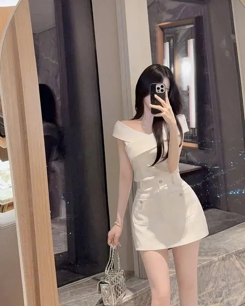 39 Trước gương ở góc phòng, cô gái diện váy kem ngắn ôm nhẹ phần thân trên, một chân trụ một chân thả làm tổng thể thanh hơn, nhìn đẹp mắt, dịu dàng và có độ mềm rất hợp với vóc dáng