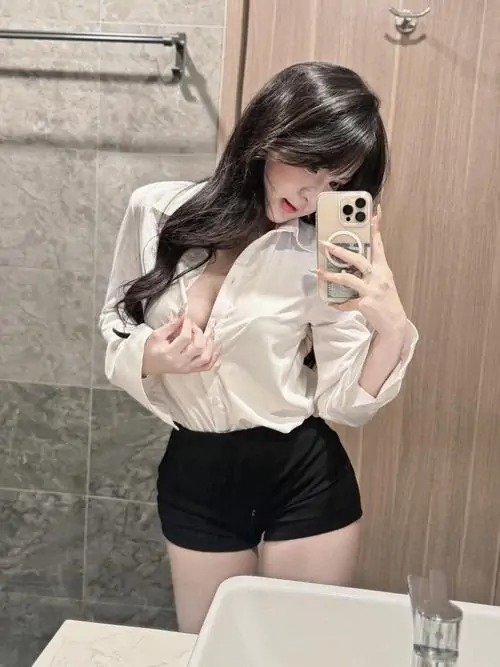 36 Gương soi trong phòng ghi lại cô nàng mặc sơ mi kem rộng phối quần ngắn đen, một tay che mặt bằng điện thoại còn tay kia buông tự nhiên, hình thể gọn xinh và mang nét sống ảo rất hợp mắt