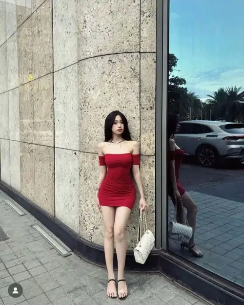 13 Hình thiếu nữ mặc váy đỏ ngắn đứng sát mảng kính lớn ngoài phố, đôi chân khép nhẹ và tóc xõa tự nhiên khiến tổng thể gọn mắt, sắc váy bắt sáng khá rõ, hợp kiểu ảnh gái xinh diện đầm ôm có thần thái nổi bật giữa bối cảnh hiện đại