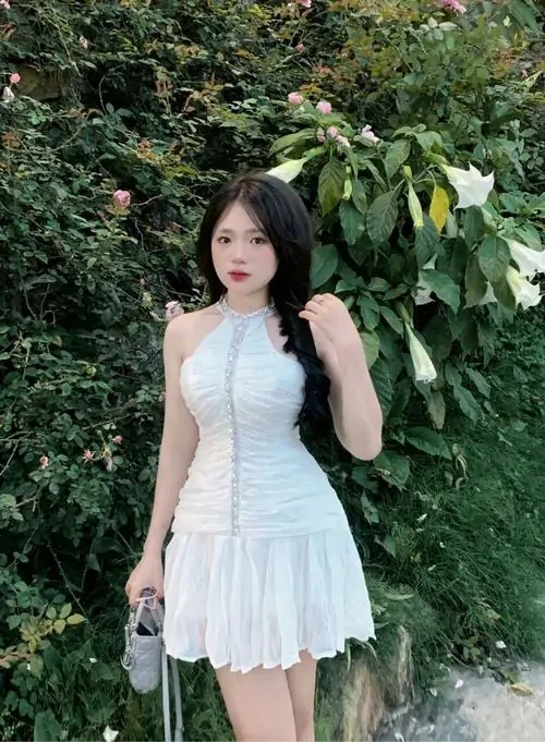 1 Ảnh gái xinh diện váy trắng xòe ngắn giữa nền lá xanh, tay cầm túi nhỏ và tóc buông nhẹ, khung hình cho cảm giác trong veo, cute và nữ tính, hợp kiểu ngắm ảnh gái đẹp mặc váy ôm theo vibe chiều hè dịu mắt