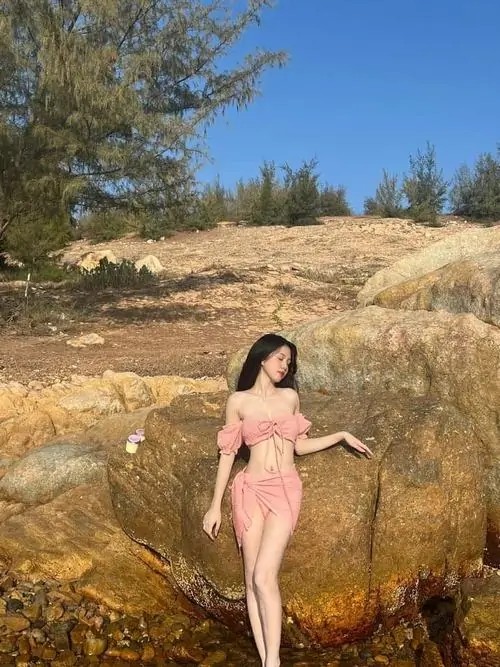 4 Tông nắng ngoài trời làm cô gái mặc đồ hồng nổi bật giữa nền đá và cỏ khô, dáng ngồi thả lỏng tạo nét mềm mại, bờ vai hiện lên rõ vừa xinh vừa sexy, hợp kiểu bộ ảnh gái đẹp mặc váy tôn dáng mang màu sắc lạ mắt