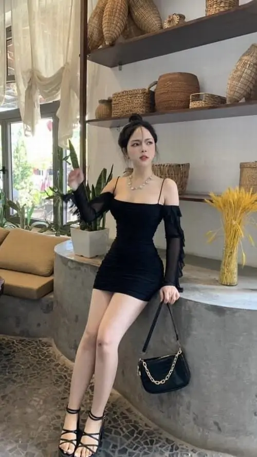 8 Cô nàng diện đầm đen ngắn trễ vai trong góc quán sáng vàng, một tay cầm túi đen, đôi sandal cao làm dáng đứng thêm gọn, cảm giác vừa cute vừa trưởng thành, lên rõ chất ôm dáng tinh tế mà không cần bày nhiều phụ kiện