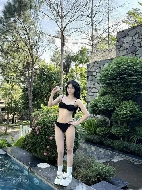 2 Cô nàng diện bikini đen đứng nghiêng trên lối đá cạnh vườn xanh khoe đôi chân thon và dáng người thanh thoát