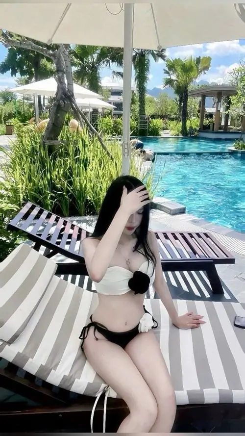 5 Người đẹp tựa lưng trên ghế sọc dưới ô trắng diện đồ tắm đen và biểu cảm thư thái bên làn nước