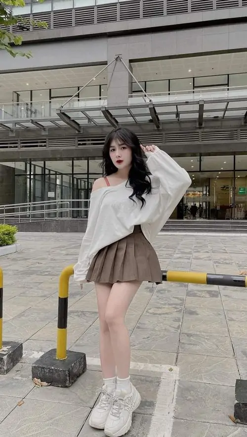 12 Cô gái mặc áo xám tay dài với chân váy ngắn đứng ở không gian đô thị, một tay đưa lên tóc làm bố cục thêm mềm, ảnh cô gái mặc đầm theo kiểu học đường này nhìn dễ thương mà vẫn cuốn