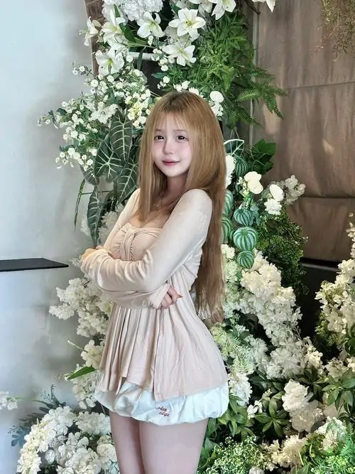 13 Ảnh cô gái mặc đầm màu kem đứng cạnh cụm hoa trắng trong nhà, chất váy rủ nhẹ và nụ cười nhỏ tạo cảm giác thơ mộng, ảnh nữ xinh trong váy này hợp gu thích vẻ đẹp ngọt và sang