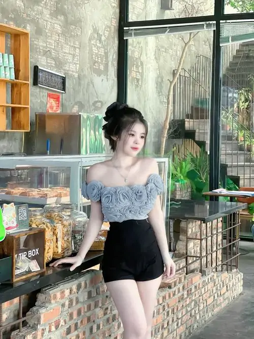 15 Hình thiếu nữ diện váy với áo xanh nhạt và chân váy đen chụp trong quán, cách đứng nghiêng bên cửa kính làm đôi chân nổi bật, khung cảnh sáng giúp ảnh gái đẹp diện váy trông hiện đại và hút mắt