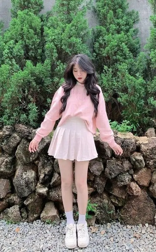 1 Ảnh gái xinh trong váy hồng phấn váy ngắn đứng trước tường đá và mảng xanh ngoài trời, dáng mở tay nhẹ làm tổng thể vừa cute vừa sexy, gương mặt sáng và vẻ mong manh nhìn rất cuốn