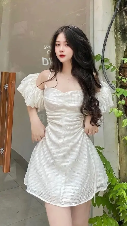 24 Cô gái mặc váy trắng ngắn đứng ở cửa ra vào, phần thân váy ôm nhẹ và mái tóc uốn lơi khiến vóc dáng nổi bật, ảnh gái đẹp diện váy này nhìn sang, đẹp và có chút lạnh lùng