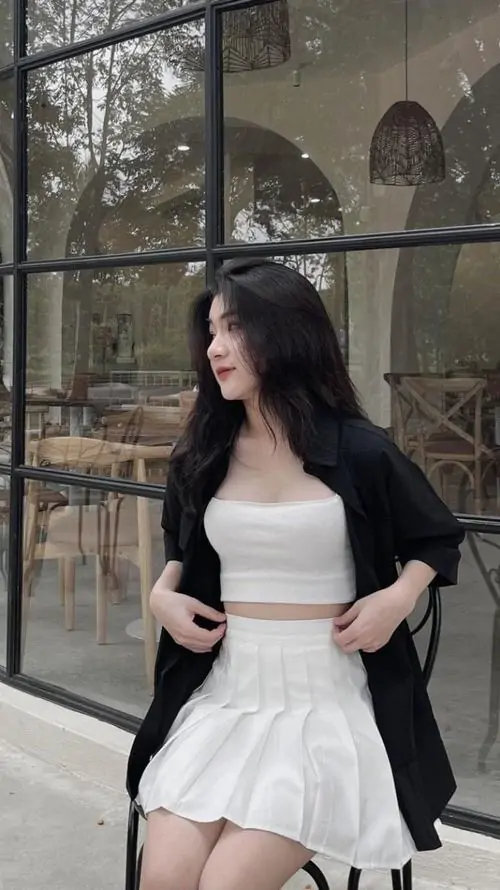 27 Ảnh gái xinh phối áo khoác đen ngoài váy trắng khi đứng cạnh khung cửa kính, tư thế nghiêng và một tay giữ áo tạo điểm nhấn cá tính, ảnh chân dung gái xinh mặc váy này vừa ngầu vừa cuốn