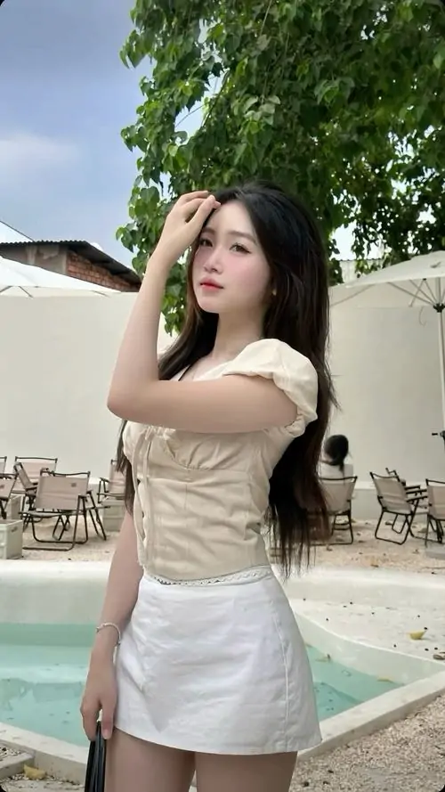 29 Hình gái đẹp trong váy trắng ôm body đứng cạnh hồ bơi xanh, một tay chạm tóc và ánh mắt hướng lên tạo vẻ kiêu kỳ, ảnh thiếu nữ diện váy này gợi cảm rõ nét mà vẫn rất đẹp