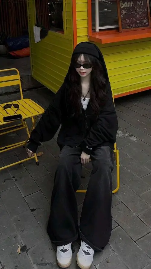 9 Gái đẹp mặc hoodie đen đứng cạnh toa tàu sắc màu với kính râm tối tạo chất riêng khó trộn giữa khung cảnh phố
