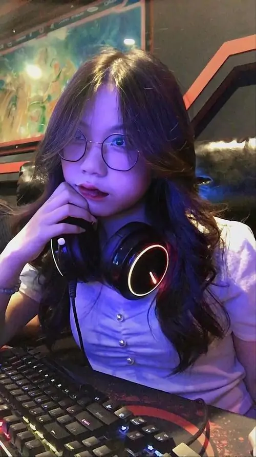 11 Ảnh cô gái ngồi trước bàn máy tính với tai nghe đặt quanh cổ, ánh đèn tím xanh phủ lên mái tóc dài và áo trắng, nàng thơ đeo kính cá tính mang vẻ năng động của góc chơi game, trẻ trung mà vẫn rất xinh