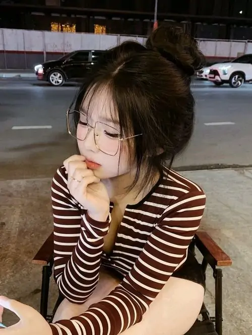 18 Cô nàng đeo kính trong bộ áo sọc nâu ngồi ở quán tối, tóc búi lơi và bàn tay chạm má tạo dáng rất mềm, ánh nhìn hướng xuống làm bức hình dịu hơn, hợp kiểu ngắm lâu vẫn thấy xinh và gần gũi