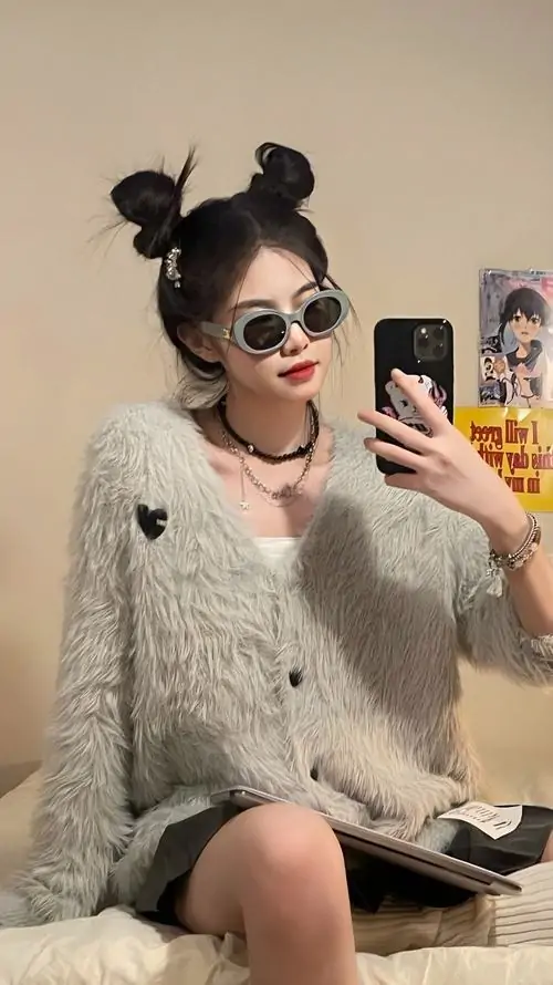 21 Ảnh gái đẹp chụp trước gương với kiểu tóc búi hai bên và kính đen, cô gái mặc áo len xám ngồi trên giường, tay cầm điện thoại, thần thái nghịch ngợm khiến khung hình trong phòng vẫn rất nổi bật và vui mắt